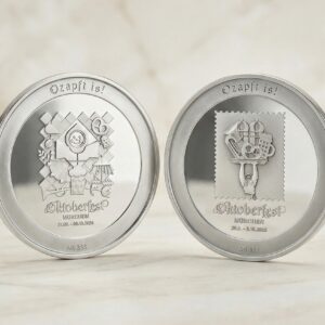 Zwei Medaillen aus Silber vor Marmorartigem Hintergrund. Auf den Medaillen sind die Oktoberfest Logos der Jahre 2024 und 2025 zu sehen.